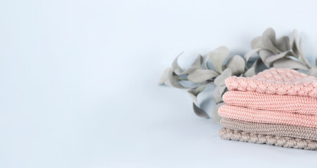Pile of pink knitted cashmere scarves, sweaters on light blue background. Folded autumn and winter clothing with eucalyptus leaves branch, banner