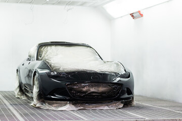 Auto body repair series: Black sports car being painted in paint booth