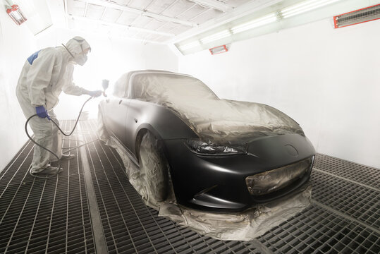 Auto body repair series: Mechanic painting black sports car in paint booth