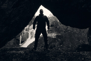 Man in the cave with waterfall i the background.