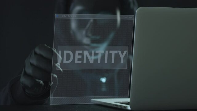 A hacker wearing black mask pulls IDENTITY tab from a laptop. Hacking concept