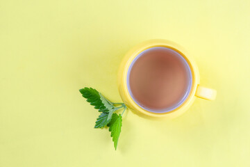 Yellow cup of hot tea with mint on yellow background, top view, flat lay