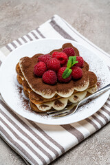 portion of Classic tiramisu dessert with raspberries on grey concrete background