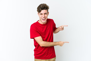 Young caucasian man isolated on white background pointing with forefingers to a copy space, expressing excitement and desire.