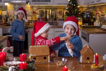 Cute children, boy brothers, decorating handmade gingerbread houses with frosting and candies