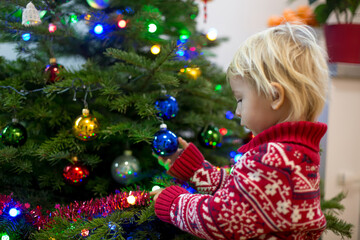 Cute little blonde boy with Christmas sweater, decorating christmas tree