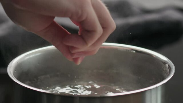 Slow Motion Man Hand Adding Salt To Boiling Water In A Saucepan Closeup