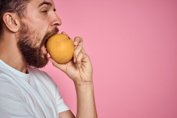 Young man with orange on a pink background in a white t-shirt emotions fun gesticulating with model hands