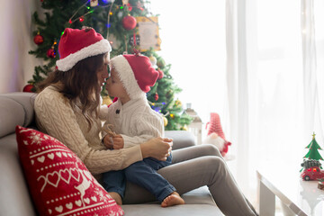 Beautiful young mom and blonde toddler boy, sitting in cozy living romm, decorated for Christmas