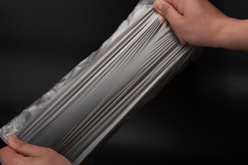 Two hands are testing the toughness of transparent plastic bags against a black background