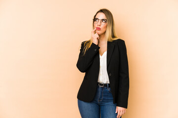 Middle age business woman isolated on beige background looking sideways with doubtful and skeptical expression.