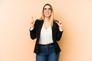 Middle age business woman isolated on beige background indicates with both fore fingers up showing...