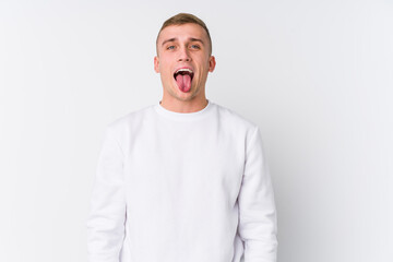 Fototapeta premium Young caucasian man on white background funny and friendly sticking out tongue.
