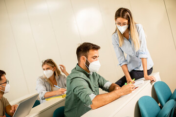 Obraz premium Female instructor wearing face protective medical mask for virus protection and helping male student at lecture hall