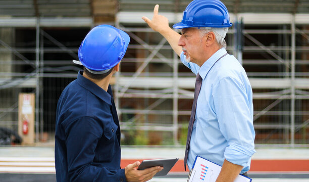 Two architect developers reviewing building plans at construction site using a tablet