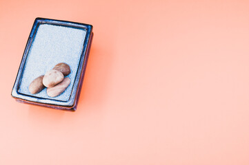 Top view of pebbles on a rectangular box filled with small blue rocks on pink background