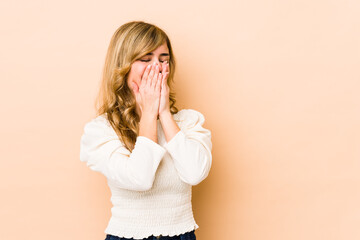 Young blonde caucasian woman laughing about something, covering mouth with hands.