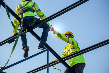 Two Asian construction workers wore safety clothing and safety harnesses to work on the steel roof...
