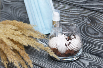 Zephyr in a glass. With biscuit and chocolate. Nearby is a medical mask, antiseptic and a bouquet of dried herbs. On pine boards painted black and white.