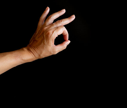 Mano con tres dedos levantados y dos haciendo un c&iacute;rculo de ok, sobre fondo negro.