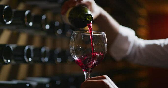 Close up shot winemaker or sommelier is pouring red wine in transparent glass for tasting a flavor and checking a quality  in a wine cellar.
