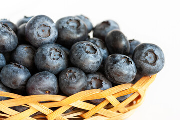 Fresh ripe blueberries in a small wicker basket on a white background. Close-up.