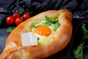 Adjarian khachapuri. Traditional meal of Georgian cuisine made of yeast dough with sulguni cheese and egg yolk served with piece of butter and herbs on the wooden board