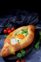 Adjarian khachapuri. Traditional meal of Georgian cuisine made of yeast dough with sulguni cheese and egg yolk served with piece of butter and herbs on the wooden board