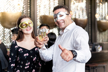 couple of young lover toasting with clinking champagne glasses at funny and happy Christmas and new year mask party atmosphere. Holiday celebrate and nightlife lifestyle concept