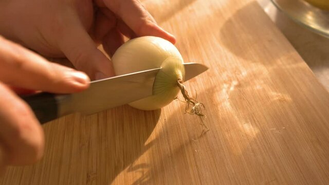 Cutting an onion into thin slices with a knife in beautiful morning light.
Eine Zwiebel wird in Scheiben geschnitten mit einem Messer im Sonnenaufgang.