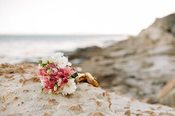 A bouquet of flowers lies on a stone on the beach.