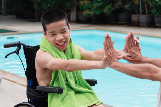 Strong Arm Muscles Of Asian Special Child On Wheelchair And Father With Swimming Pool Background, They Are Happiness In Holidays With Family Time On The Travel,Lifestyle Of Happy Disabled Kid Concept.