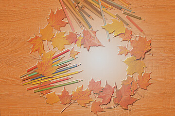 Illustration with pencils and maple leaves on a wooden table with an embossing effect on an orange ocher surface.