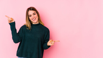 Young caucasian woman isolated on pink background pointing to different copy spaces, choosing one of them, showing with finger.