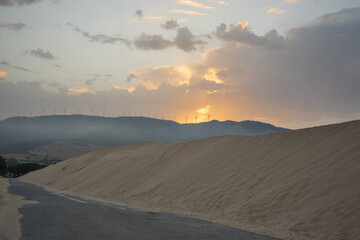 Road with dunes. Windmills on a mountain at dawn. Renewable energy concept.