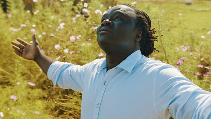 Happy african man with outstretched hands enjoying beautiful nature on the meadow or farm. High quality photo