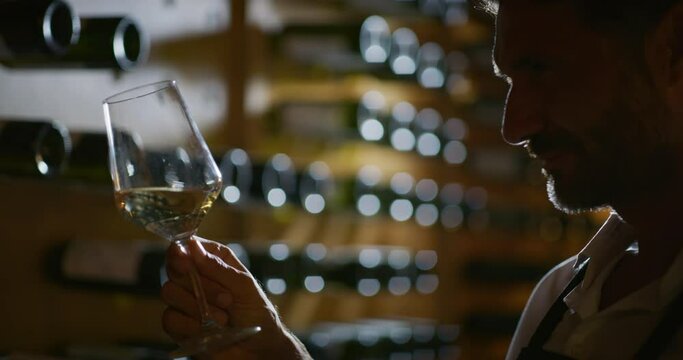 Authentic shot of happy successful male winemaker or sommelier is tasting a flavor and checking red wine quality poured in transparent glass  in a wine cellar.
