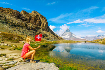 Woman with Swiss flag at Mount Matterhorn or Monte Cervino or Mont Cervin, reflected on Riffelsee...