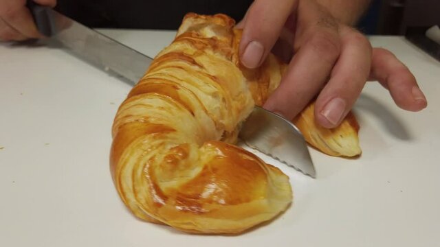 pastry chef cutting through the mitas a freshly made artisan croissant to show off the puff pastry inside