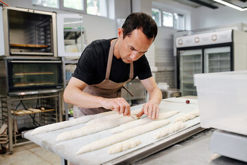 Keen male baker making baguettes on a flowered table in a kitchen