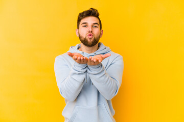 Fototapeta premium Young caucasian man isolated on yellow background folding lips and holding palms to send air kiss.