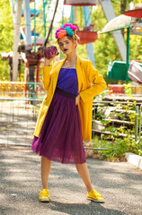 Young beautiful model in stylish clothes posing against the backdrop of attractions in an amusement park