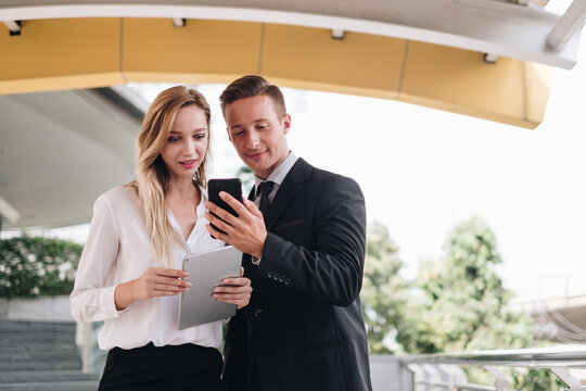 two businesspeople using a digital tablet and smartphone together in front of office