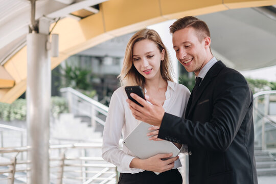 two businesspeople using a digital tablet and smartphone together in front of office