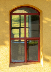 Window on a yellow  wall of a chapel. Another window on the opposite side makes you see through the building.