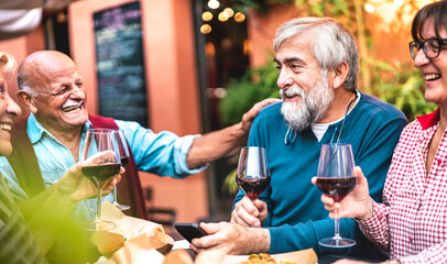 Happy senior friends having fun drinking red wine at dinner party - Retired people eating at...