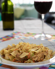 pasta with zucchini carrot and filet mignon with a glass of wine and a bottle of olive oil in the background