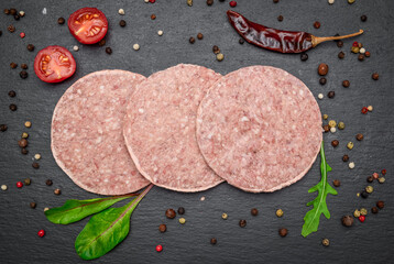 Raw burgers on paper. On black rustic background