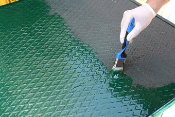 Painter renewing green paint on a metal plate