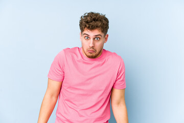 Fototapeta premium Young blond curly hair caucasian man isolated shrugs shoulders and open eyes confused.